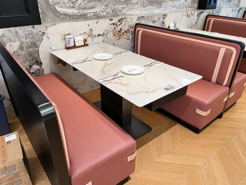 Pink upholstered restaurant booth seating with black frame and light tabletop.